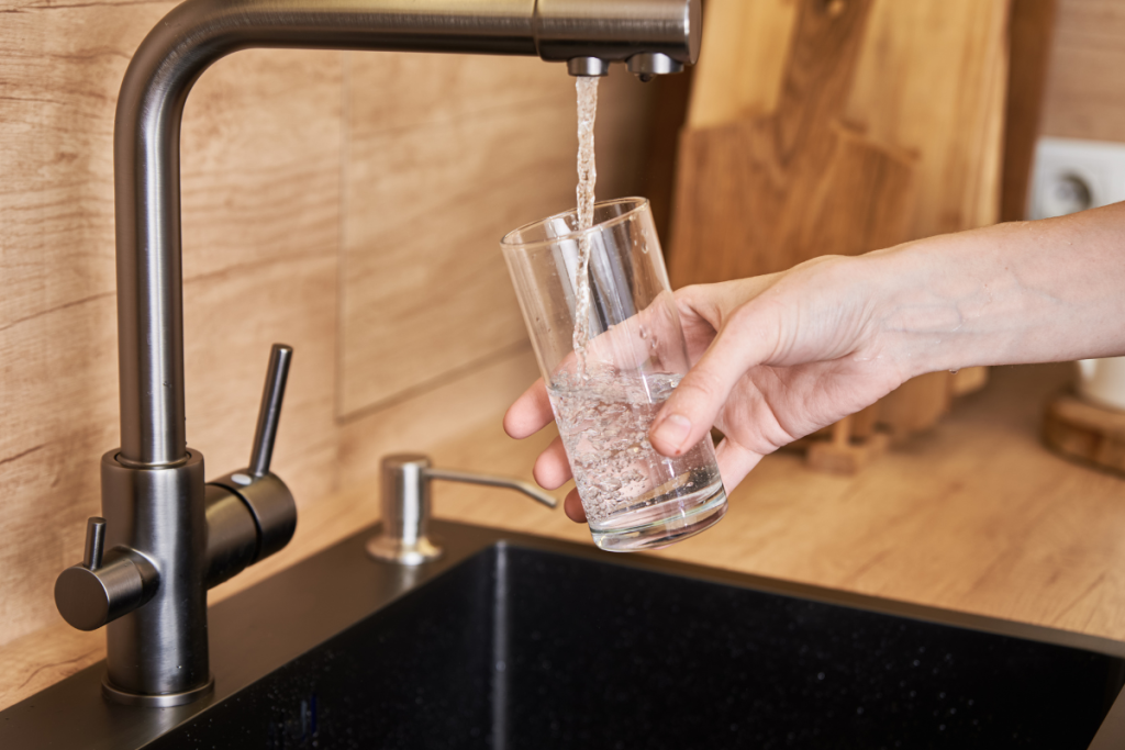A woman pours clean water from a tap into a glass.
