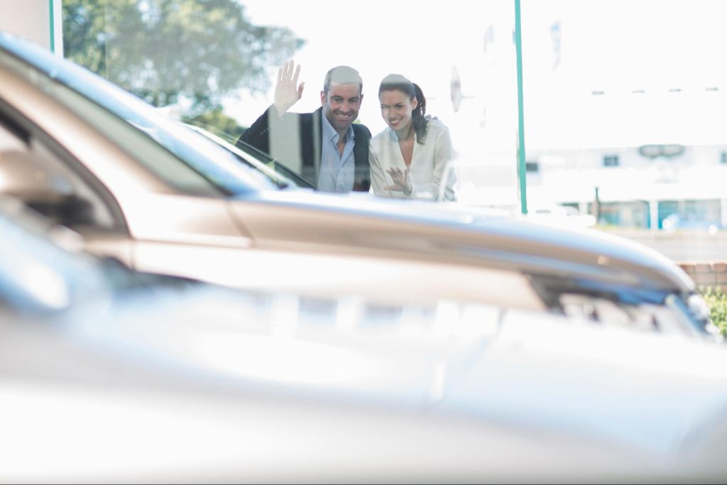 Couple leaning against dealership windows and looking at car