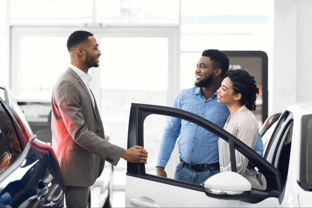 Car salesman touching door of vehicle while talking to couple