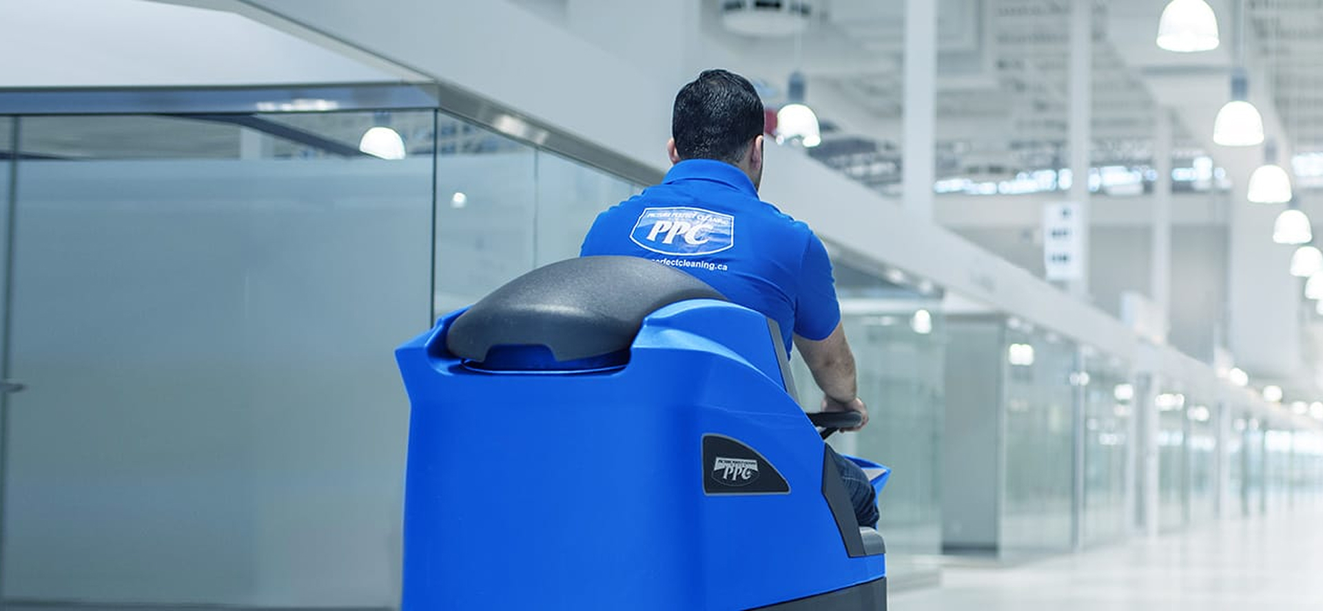Picture Perfect Cleaning staff using a blue ride-on floor scrubber to clean a large retail or mall corridor.