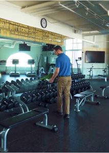Picture Perfect Cleaning team member disinfecting gym dumbbells and fitness equipment in Calgary or Edmonton.