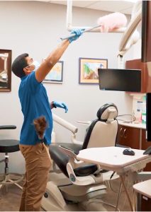 Picture Perfect Cleaning team member dusting high-touch areas in a dental clinic exam room.