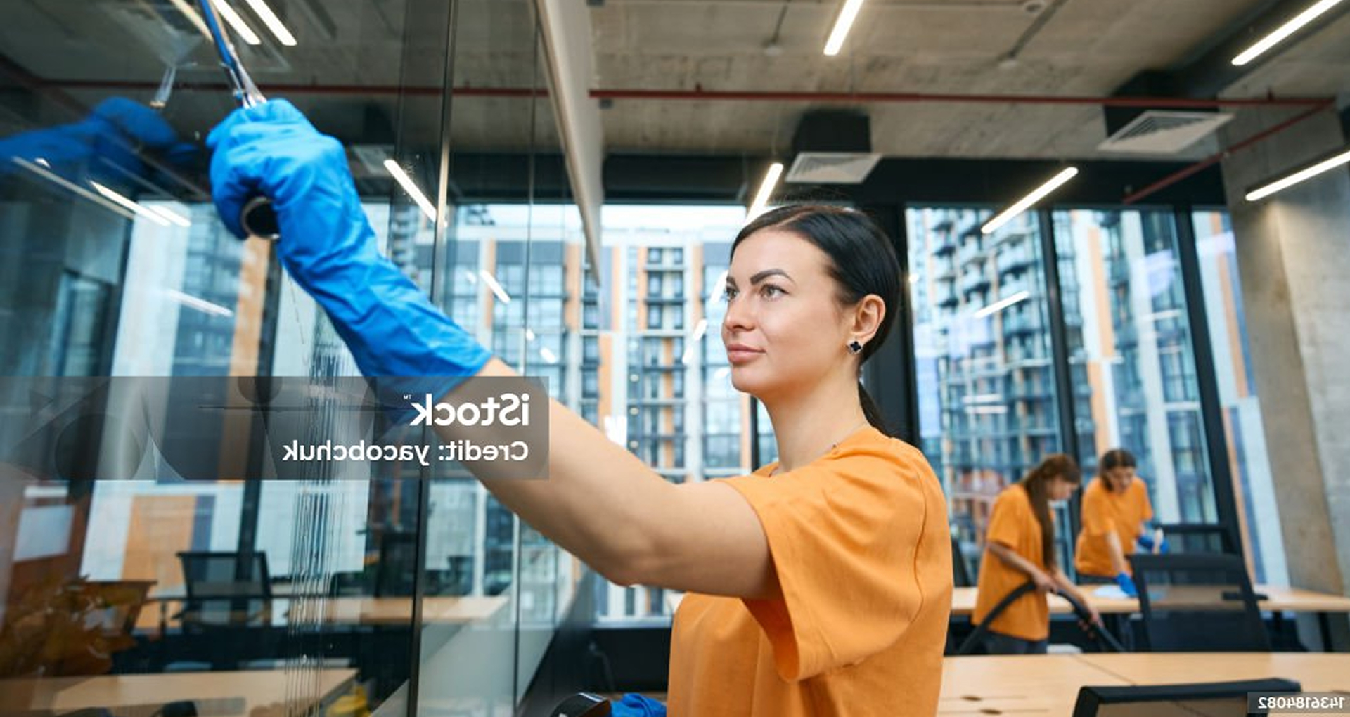 Female janitor cleaning glass in a modern condo building, part of a professional apartment cleaning team in Calgary and Edmonton