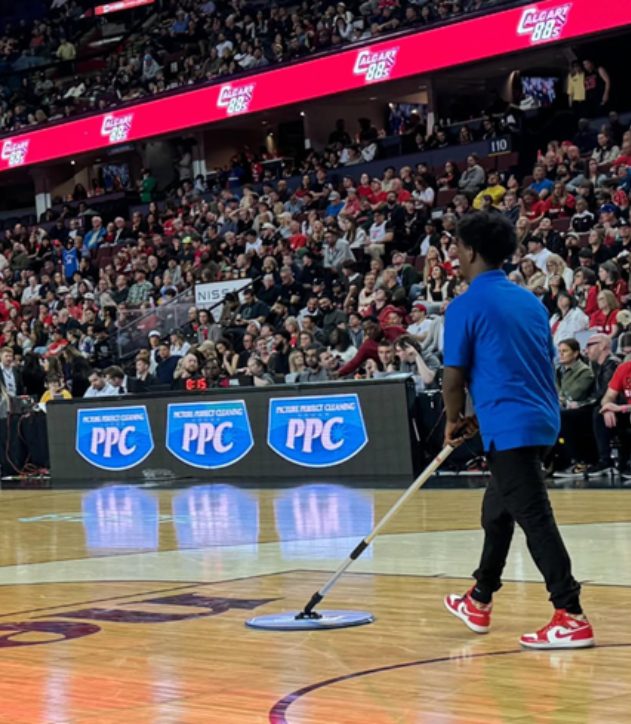 PPC staff cleaning the basketball court during a Calgary Surge game, with Picture Perfect Cleaning logos on the LED boards.