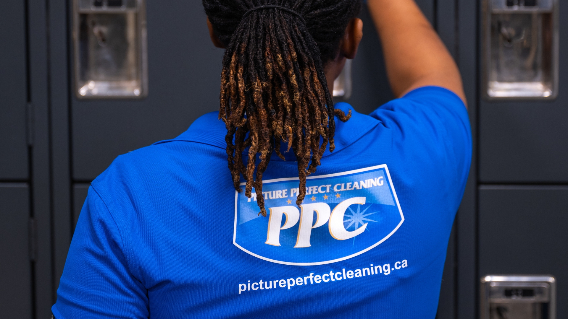 Picture Perfect Cleaning team member wearing blue uniform and gloves, disinfecting lockers in a commercial facility in Calgary or Edmonton.