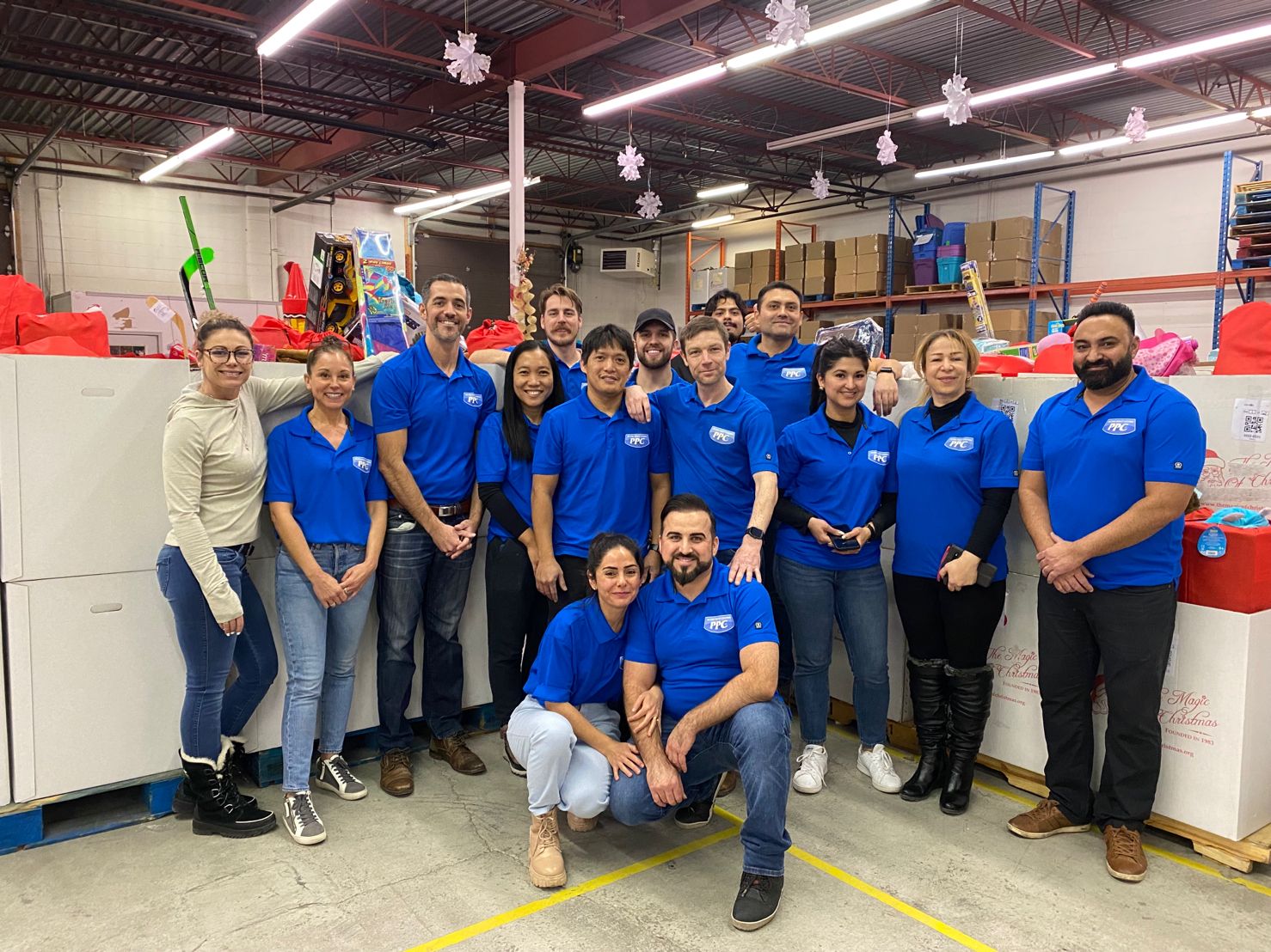 Picture Perfect Cleaning team in blue shirts volunteering at The Magic of Christmas warehouse surrounded by red gift bags.