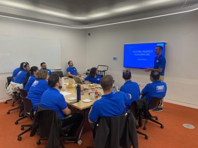 Picture Perfect Cleaning team gathered in a meeting room, discussing full-time employee health benefits with a presentation on screen.
