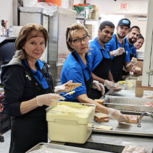 Picture Perfect Cleaning staff wearing blue uniforms and gloves while preparing sandwiches in a commercial kitchen.