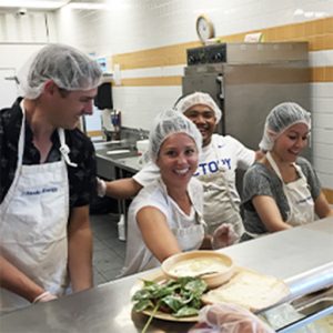 Picture Perfect Cleaning team members volunteering in a kitchen, wearing hairnets and aprons while preparing and serving food.