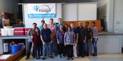 Picture Perfect Cleaning team standing in front of a Feed the Hungry banner after volunteering at a community food service event.